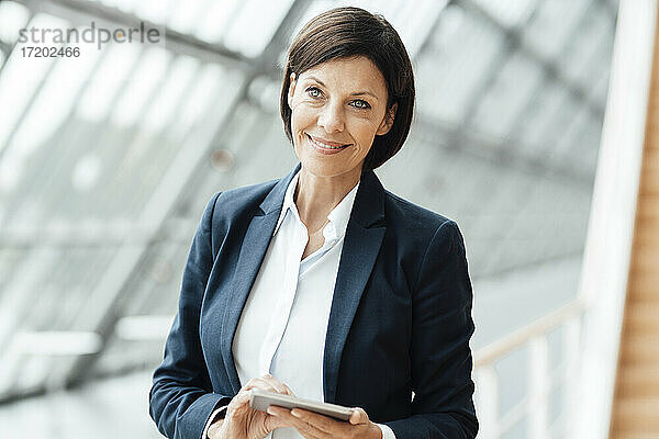 Lächelnde Geschäftsfrau mit digitalem Tablet im Korridor