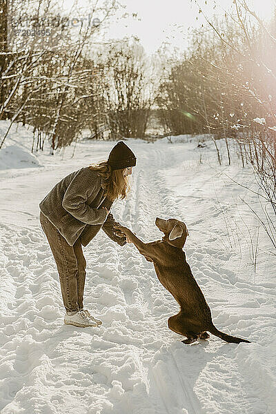 Teenager-Mädchen spielt mit Hund im Schnee in der Winterdämmerung