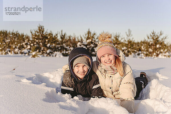 Cute Geschwister liegen auf Schnee gegen den Himmel bei Sonnenuntergang