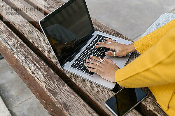 Frau benutzt Laptop auf einer Bank sitzend
