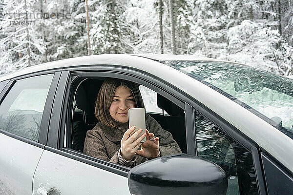 Junge Frau fotografiert im Auto sitzend mit dem Handy