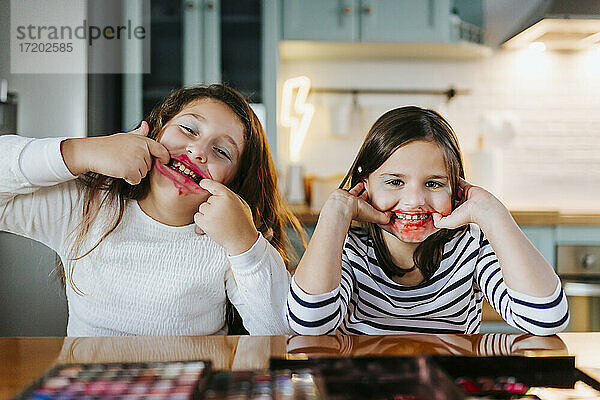 Playful Mädchen mit Make-up auf Gesicht necken  während am Esstisch in der heimischen Küche sitzen
