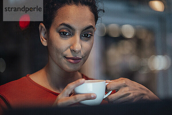 Junge Frau trinkt Kaffee  während sie in einem Café sitzt und auf ihren Laptop schaut