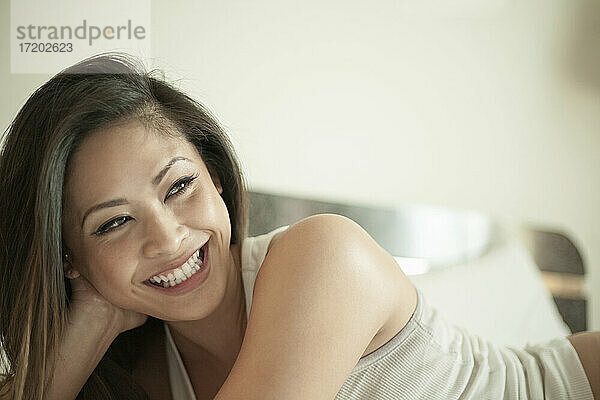 Lächelnde Frau  die wegschaut  während sie zu Hause auf dem Bett liegt