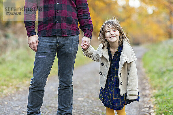 Nettes Mädchen lächelt  während sie die Hand ihres Vaters im Wald hält