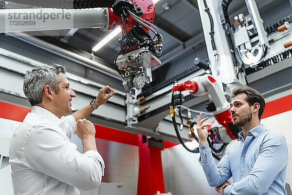 Lächelnde Automatisierungsingenieure diskutieren über einen Roboterarm in einer Fabrik