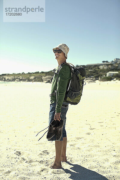Männlicher Tourist mit Rucksack auf Sand stehend an einem sonnigen Tag