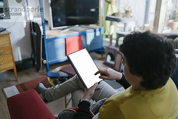 Mittlerer Mann  der ein digitales Tablet benutzt  während er zu Hause auf dem Sofa sitzt