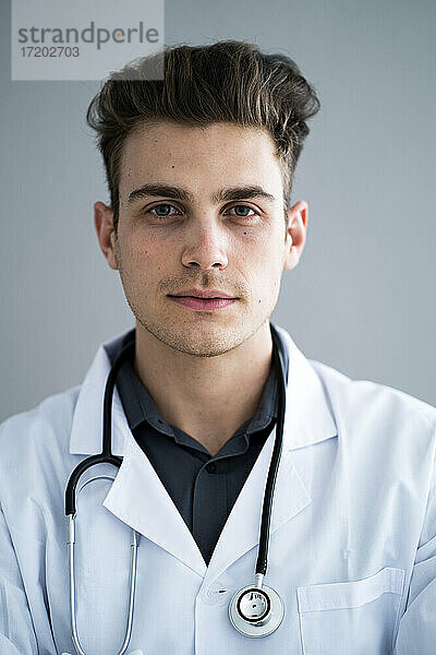 Hübscher männlicher Arzt vor grauer Wand im Krankenhaus