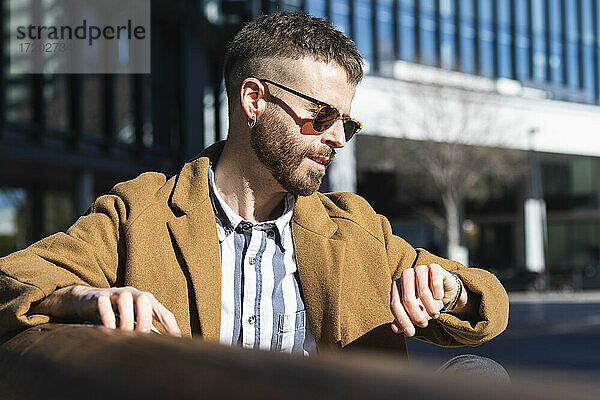 Geschäftsmann prüft die Zeit  während er an einem sonnigen Tag auf einer Bank sitzt