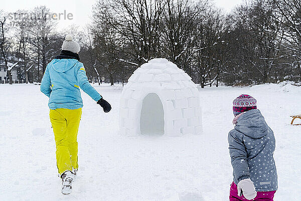 Verspielte Mutter und Tochter laufen im öffentlichen Park bei Schnee