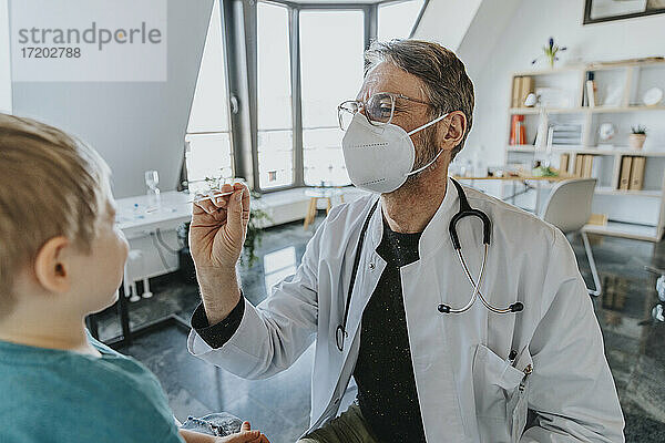 Männlich  mit Gesichtsschutzmaske  Kinderarzt  der einen Nasenabstrich bei einem Jungen macht  während er in der Klinik steht