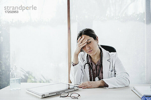 Besorgte weibliche medizinische Fachkraft mit dem Kopf in der Hand sitzt am Schreibtisch im Krankenhaus