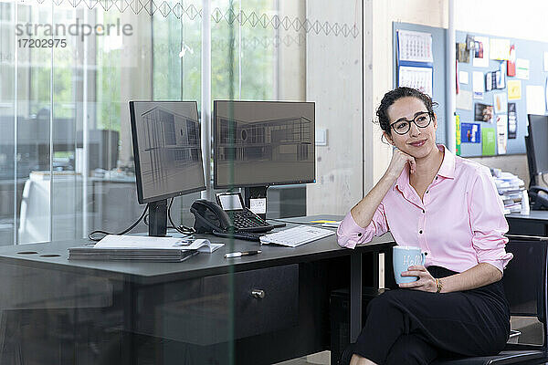 Nachdenkliche Geschäftsfrau mit Kaffeetasse am Schreibtisch sitzend im Büro