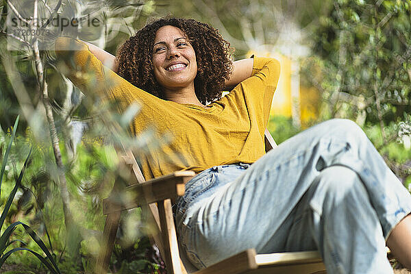 Lächelnde Frau  die sich im Frühling im Gartenstuhl in einem nachhaltigen Bio-Gemüsegarten entspannt