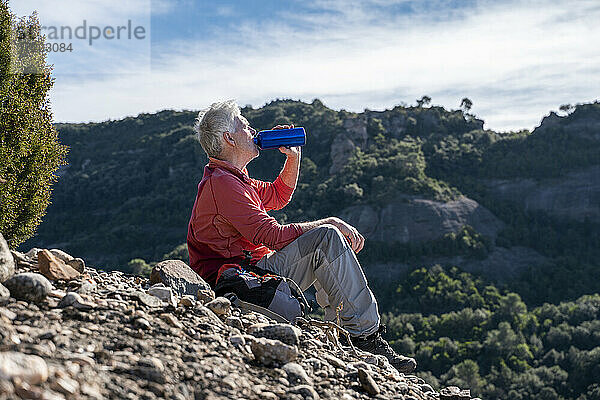 Männlicher Wanderer trinkt Wasser  während er auf einem Berg bei Sant Llorenc del Munt i l'Obac  Katalonien  Spanien  sitzt