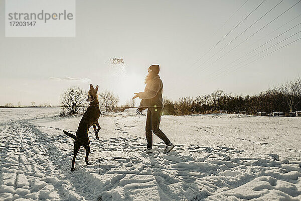 Teenager-Mädchen spielt mit Hund im Schnee bei Wintersonnenaufgang