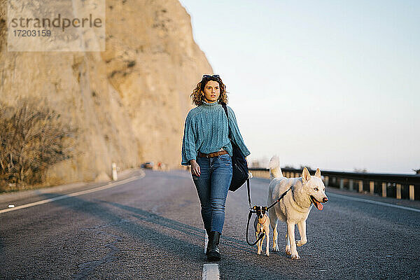 Frau mit Siberian Husky und Jack Russell Terrier schaut weg  während sie auf einer Bergstraße spazieren geht