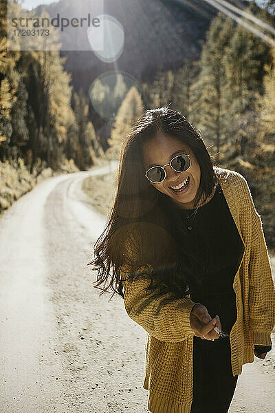 Junge Frau mit Sonnenbrille und Zigarette in der Hand auf einem Waldweg