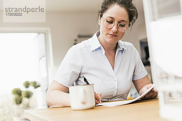 Berufstätige Frau mit Brille  die am Schreibtisch sitzend ein Dokument bearbeitet