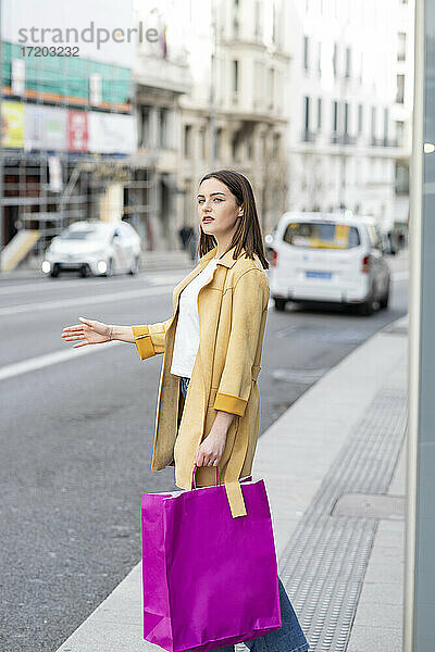 Frau mit Einkaufstaschen  die auf dem Bürgersteig stehend ein Taxi ruft
