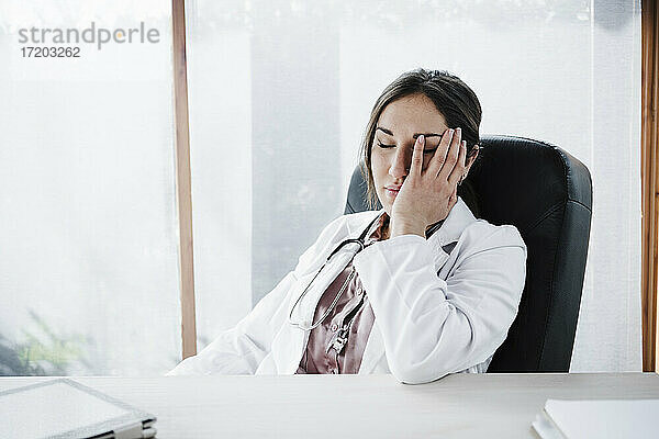 Müde Ärztin mit geschlossenen Augen am Schreibtisch sitzend