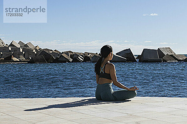 Junge Frau meditiert auf der Promenade an einem sonnigen Tag