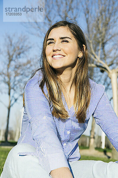 Lächelnde Frau  die wegschaut  während sie im Park sitzt
