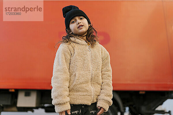 Nettes Mädchen mit Strickmütze und Pullover  das vor einem roten Lastwagen steht