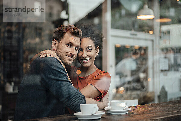 Paar lächelnd  während umarmt einander beim Sitzen im Café