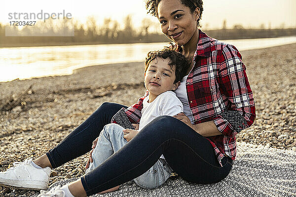 Lächelnde Mutter sitzt mit ihrem Sohn auf einer Decke am See