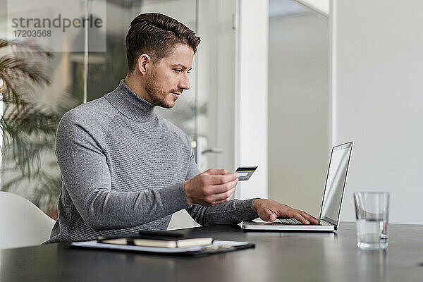 Geschäftsmann  der online mit Kreditkarte auf einem Laptop im Büro bezahlt