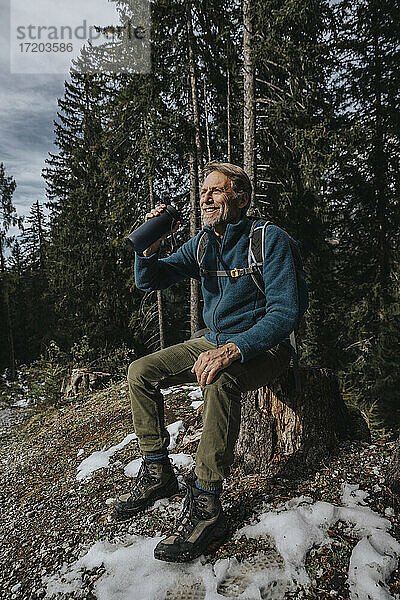 Lächelnder männlicher Tourist  der eine Wasserflasche in der Hand hält  während er im Wald im Salzburger Land  Österreich  sitzt