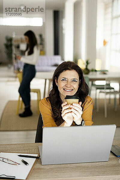 Lächelnde Geschäftsfrau mit Kaffeetasse bei der Arbeit zu Hause