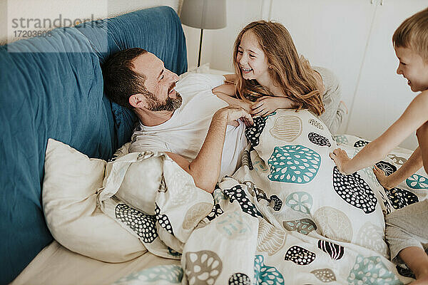 Lächelnde Tochter und Sohn haben Spaß mit Vater auf dem Bett zu Hause