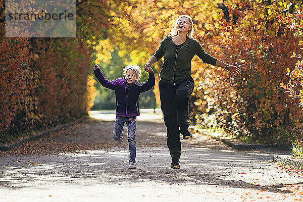 Mutter und Tochter halten sich an den Händen und laufen im Herbst im Park