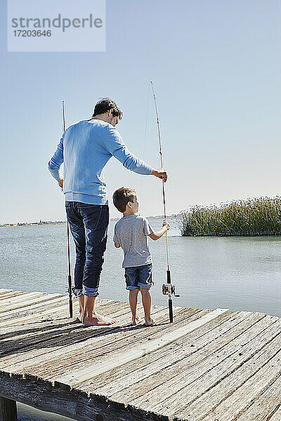 Vater und Sohn halten die Angelrute  während sie am Pier stehen
