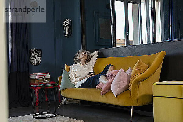 Ältere Frau mit digitalem Tablet entspannt sich auf dem Sofa zu Hause