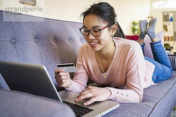 Junge Frau mit Kreditkarte  die lächelnd einen Laptop zu Hause benutzt