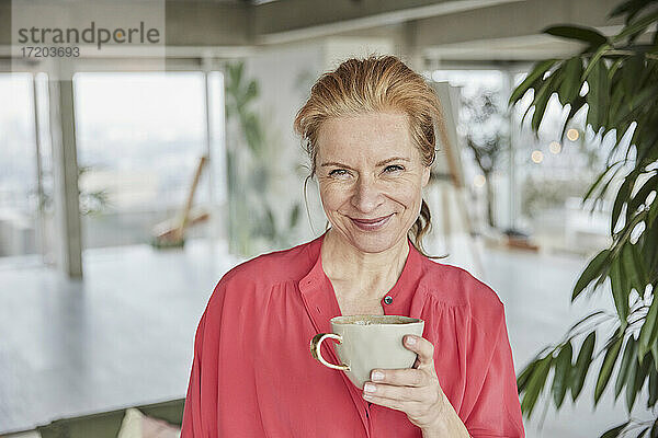 Lächelnde reife Frau hält Kaffeetasse zu Hause