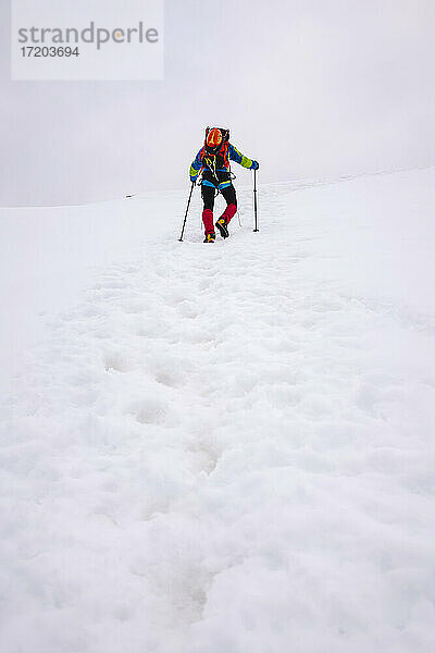 Männlicher Wanderer  der einen schneebedeckten Berg mit Wanderstöcken besteigt