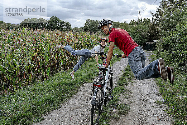 Älterer Mann mit Tochter  die auf einem landwirtschaftlichen Feld auf dem Fahrrad hüpft