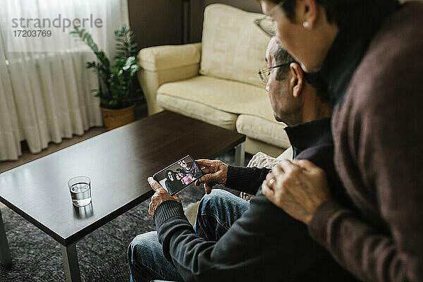 Ein älterer Mann und eine ältere Frau führen während der COVID-19 einen Videogespräch mit ihrer Familie über ihr Smartphone zu Hause