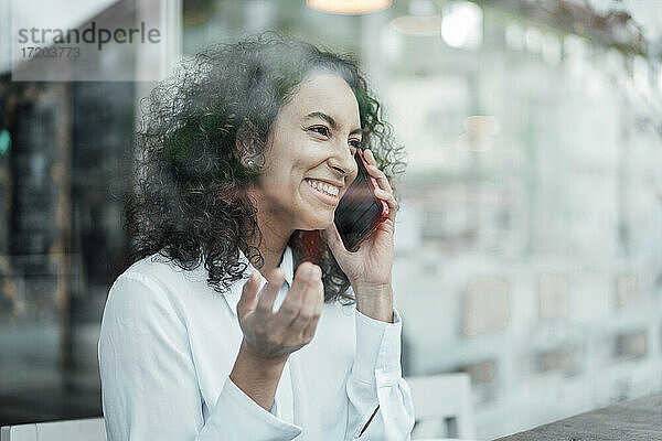 Junge Geschäftsfrau lächelt  während sie in einem Café sitzt und mit ihrem Handy spricht