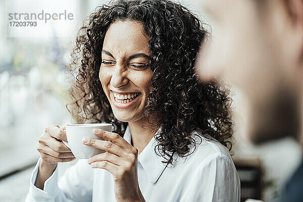 Fröhliche Geschäftsfrau  die mit einem Kollegen Kaffee trinkt  während sie in einem Cafe sitzt