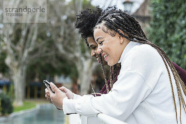 Lächelnde Frau  die ein Mobiltelefon benutzt und neben einem Jungen im Freien steht
