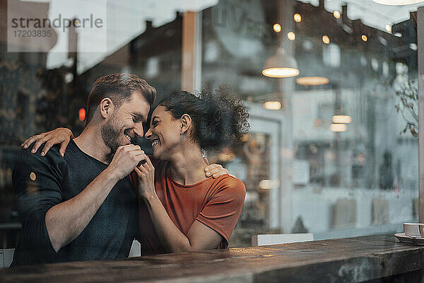 Paar sitzt lächelnd mit Arm um einander im Café
