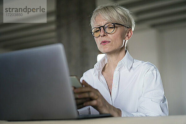 Geschäftsfrau mit Laptop und Smartphone im Home Office sitzend