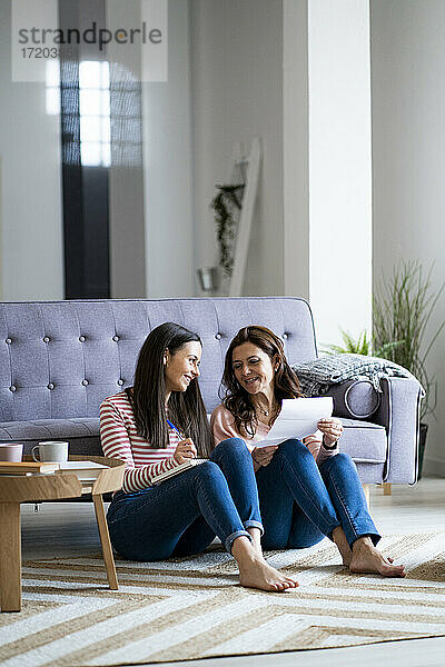 Tochter und Mutter prüfen Rechnungen  während sie auf dem Sofa im Wohnzimmer sitzen