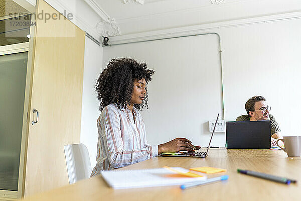Junge Unternehmerin mit einem männlichen Kollegen  der an einem Laptop arbeitet  während er im Sitzungssaal im Büro sitzt